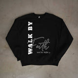 Black sweatshirt with 'Walk by Faith not by Sight' text on a beige surface